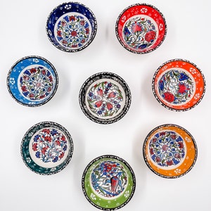 May include: Eight small ceramic bowls with intricate floral designs in various colors, including blue, red, green, and orange. The bowls have black outlines and white backgrounds.