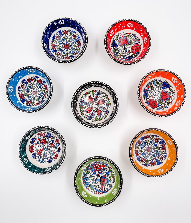 May include: Eight small ceramic bowls with intricate floral designs in various colors, including blue, red, green, and orange. The bowls have black outlines and white backgrounds.