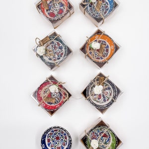 May include: Ten small ceramic bowls with colorful Turkish designs are packaged in clear boxes with brown paper and twine. Each bowl has a small white flower and a tag with the text "Bella & David 15.08.2021 Love"