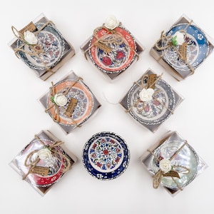 May include: Eight small ceramic bowls with colorful floral patterns, packaged in clear boxes with brown paper and twine. Each bowl has a small tag with the text "Gabella & David 15.09.2021 with love".