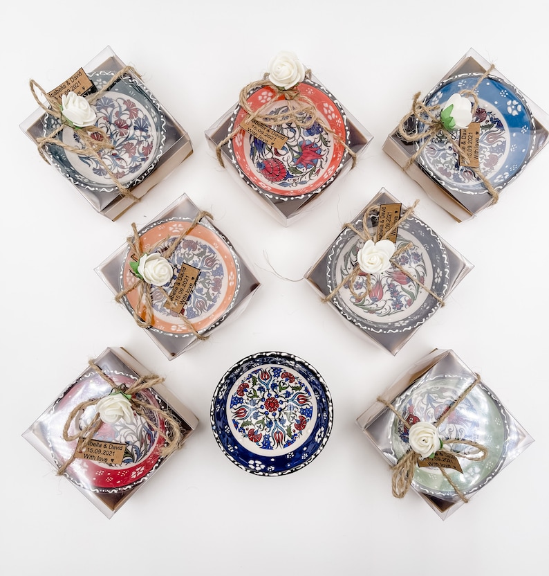 May include: Eight small ceramic bowls with colorful floral patterns, packaged in clear boxes with brown paper and twine. Each bowl has a small tag with the text "Gabella & David 15.09.2021 with love".