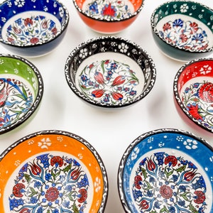 May include: Set of eight small ceramic bowls with intricate floral designs in shades of blue, green, red, and orange. The bowls have a white background with black trim.