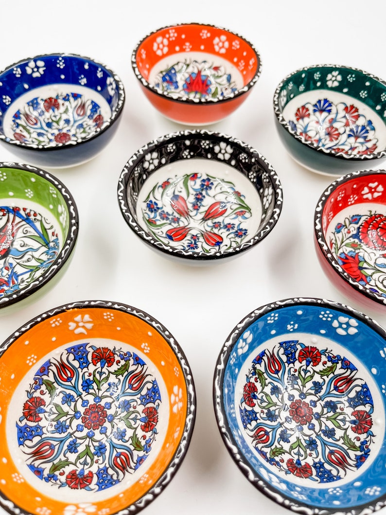 May include: Set of eight small ceramic bowls with intricate floral designs in shades of blue, green, red, and orange. The bowls have a white background with black trim.