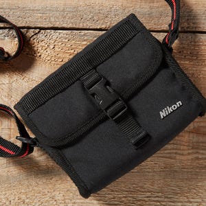 May include: Black Nikon camera case with a black and red striped strap. The case has a buckle closure and the Nikon logo is visible on the front. The case is made of a durable material and is designed to protect a camera.