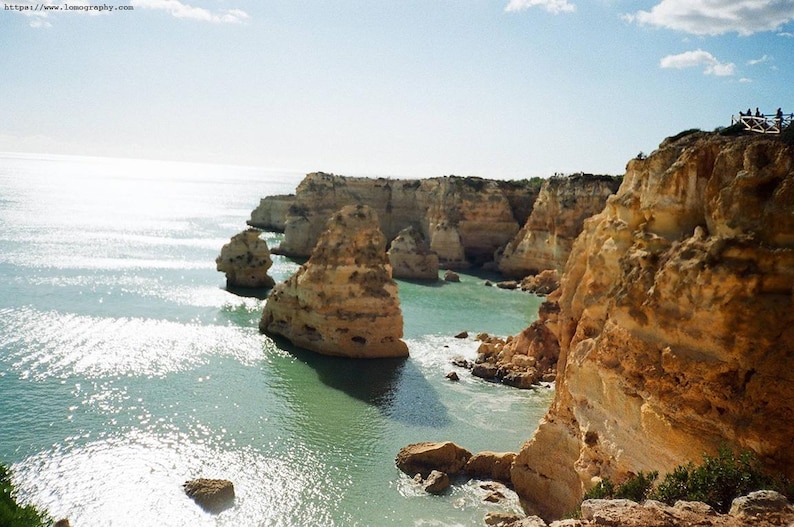May include: Coastal landscape featuring a turquoise sea and towering, weathered rock formations. The image captures a sunny day with a clear blue sky, highlighting the natural beauty of the cliffs and water. The scene evokes a sense of tranquility and the power of nature.