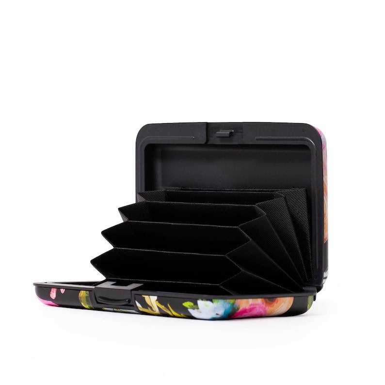Peut inclure: Un porte-cartes en aluminium noir et &agrave; motifs floraux avec un int&eacute;rieur noir et plusieurs fentes pour cartes. Le porte-cartes est ouvert et les fentes sont visibles.