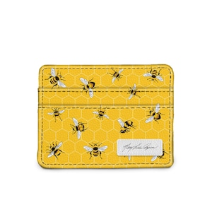 May include: Yellow leather card holder with a honeycomb pattern and black and yellow bees. The card holder has a white label with the text "Mary Kate Aspen" in black cursive.