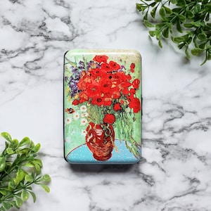 May include: A red and green card holder with a painting of a vase of red poppies. The vase is brown and the background is green.