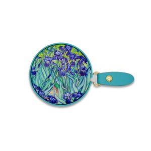 May include: A round hand mirror featuring a print of Van Gogh's "Irises" painting. The mirror has a teal border and a matching teal handle with a gold-colored metal clasp. The artwork showcases blue irises and green foliage.