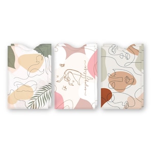 May include: Set of three card holders with abstract line art designs. The first card holder features a green leaf and a brown abstract shape. The second card holder features a woman in a yoga pose with the text "enjoy life". The third card holder features a brown abstract face.