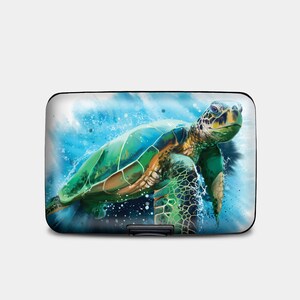 May include: A black metal card holder with a colorful image of a sea turtle swimming in blue water with white splashes.