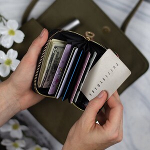 May include: A small black zippered wallet with a floral pattern. The wallet is open and contains cash, credit cards, and a blank card with the word "POLLITHANNA" written on it.