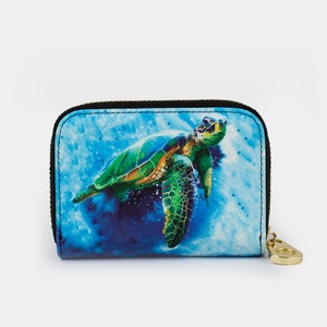 May include: A small blue and green zippered wallet with a colorful sea turtle design. The turtle is swimming in a blue and white watercolor background.