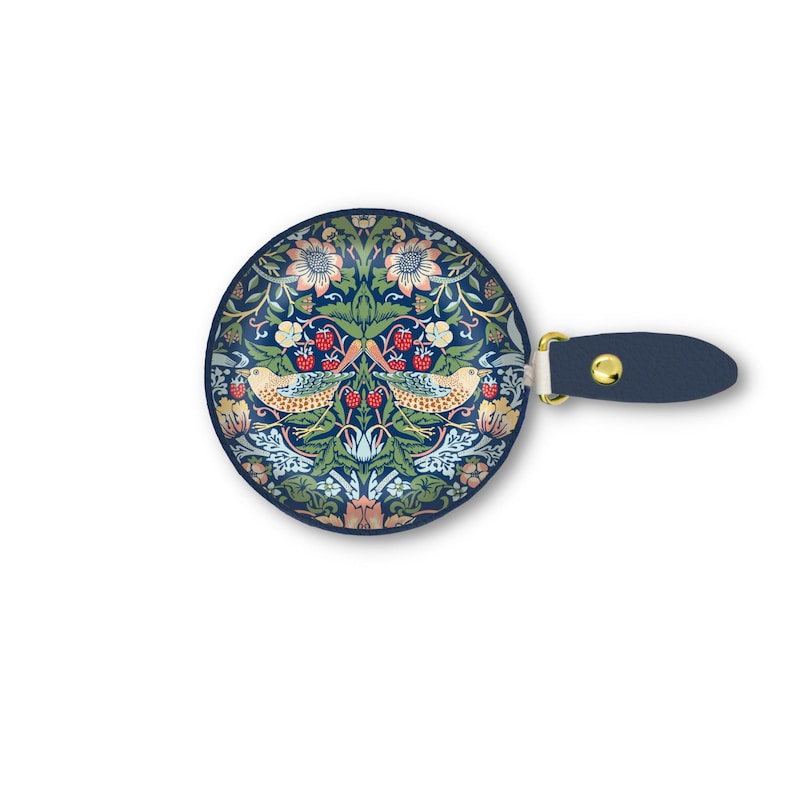 K&ouml;nnte beinhalten: Ein runder, marineblauer Handspiegel mit einem dekorativen Blumen- und Vogeldesign. Das Design zeigt V&ouml;gel, Blumen und Beeren in Gr&uuml;n-, Rosa- und Gelbt&ouml;nen. Der Griff ist aus marineblauem Leder mit einem goldfarbenen Metallakzent.