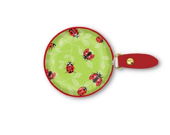 May include: A round, hand-held mirror with a red border and a red handle. The mirror's face features a light green background with a pattern of red ladybugs and white leaves. The handle is attached with a gold-colored metal piece.