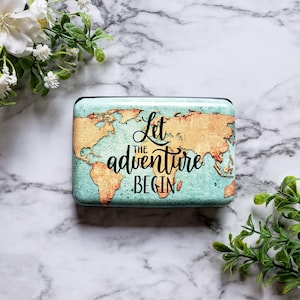 May include: A black card holder with a world map design and the text "Let the adventure begin".