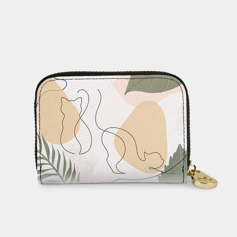 May include: A white zippered wallet with a black zipper pull. The wallet features a pattern of abstract shapes in beige and green, with a line drawing of two cats.