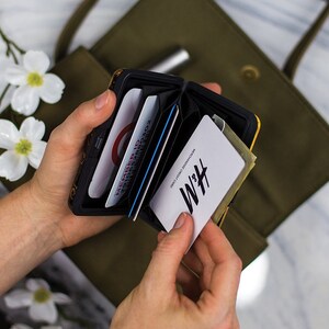 May include: A black and yellow metal card holder with a floral pattern. The card holder is open and shows several cards, including a white card with the text "H&M" and "REWARDS CREDIT CARD".