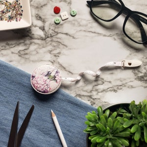 May include: A white ceramic mug with a black handle and the text "But First, Coffee" in a bold, black font. The mug is filled with a dark liquid, likely coffee, and sits on a light-colored surface.