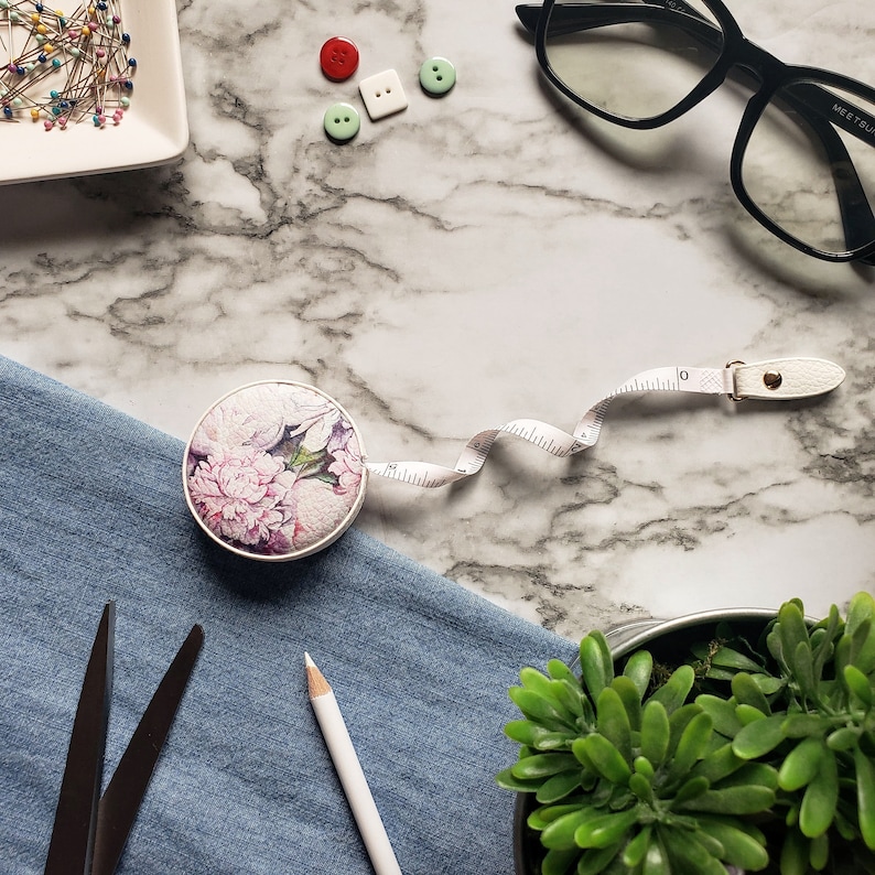 May include: A white ceramic mug with a black handle and the text "But First, Coffee" in a bold, black font. The mug is filled with a dark liquid, likely coffee, and sits on a light-colored surface.