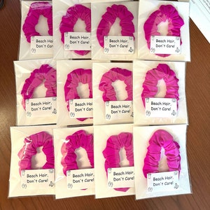 May include: Twelve pink hair scrunchies with the text "Beach Hair, Don't Care!" on white labels.