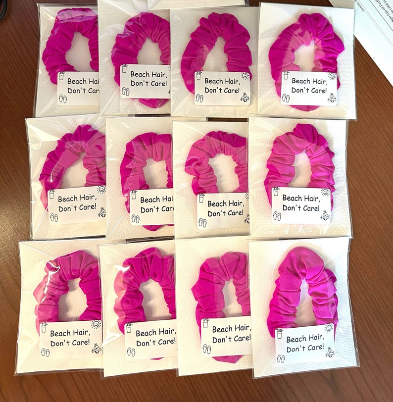 May include: Twelve pink hair scrunchies with the text "Beach Hair, Don't Care!" on white labels.