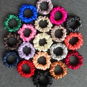 May include: A collection of 20 colourful scrunchies made of silky fabric. The scrunchies are arranged in a circle on a grey textured surface.