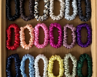 May include: A collection of 20 colorful, silky scrunchies arranged in three rows. The scrunchies are made of a soft, stretchy fabric and come in a variety of colors, including black, white, red, pink, blue, green, yellow, and brown.
