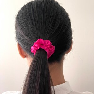 May include: A person with long black hair tied back with a bright pink scrunchie.