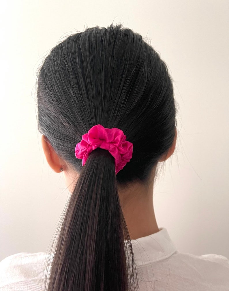 May include: A person with long black hair tied back with a bright pink scrunchie.