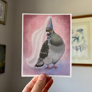 Könnte beinhalten: Quadratischer Kunstdruck mit einer Aquarellillustration einer Taube mit blauem Partyhut und weißem Schleier. Die Taube ist grau und weiß mit orangefarbenen Füßen, vor einem rosa-violetten Hintergrund.