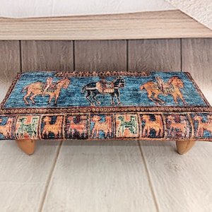 Può includere: Uno sgabello blu e arancione con motivo a quattro gambe in legno. Lo sgabello presenta un motivo ripetitivo di cavalli e cavalieri.