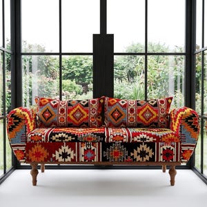 May include: A two-seater sofa with a vibrant, patterned fabric in red, yellow, black, and blue geometric designs. The sofa has a wooden frame and two matching throw pillows. The design is reminiscent of Southwestern or tribal art.
