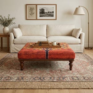May include: A square ottoman featuring a vibrant orange and red fabric with a stylized tree print, supported by four dark brown turned wooden legs. A rectangular wooden tray sits on top, holding two stacked books and a white ceramic mug.