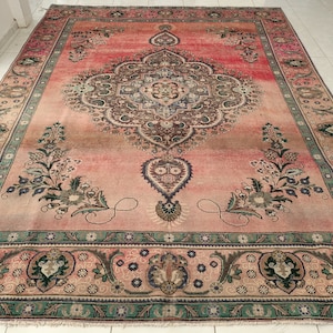 May include: A vintage Persian rug with a pink background and intricate floral patterns in shades of green, brown, and blue. The rug has a central medallion and a border with repeating motifs.