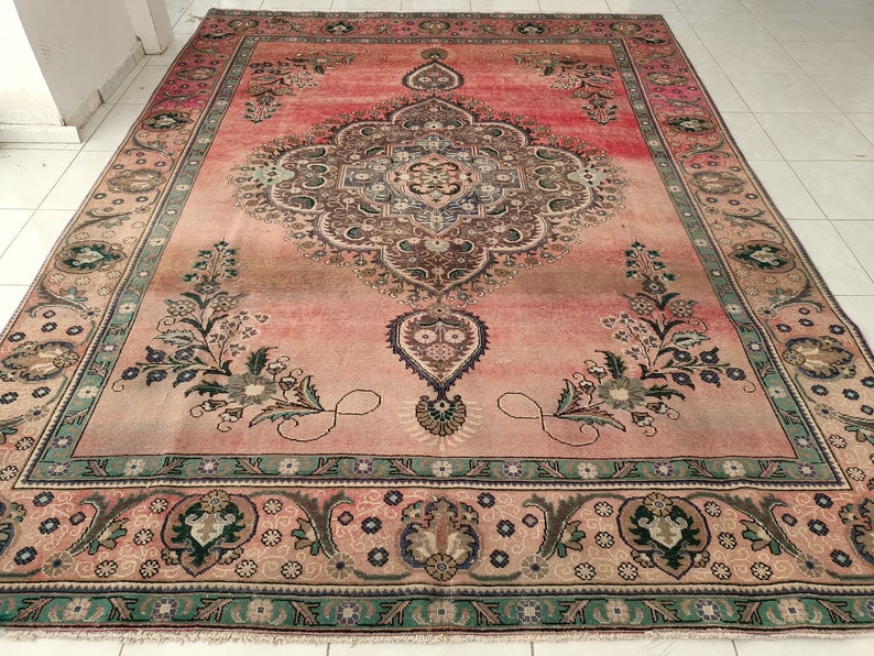 May include: A vintage Persian rug with a pink background and intricate floral patterns in shades of green, brown, and blue. The rug has a central medallion and a border with repeating motifs.