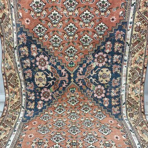 May include: A vintage rug with a traditional Persian design. The rug features a central medallion with intricate floral patterns in shades of red, blue, and cream. The rug has a faded, worn look, adding to its antique charm.