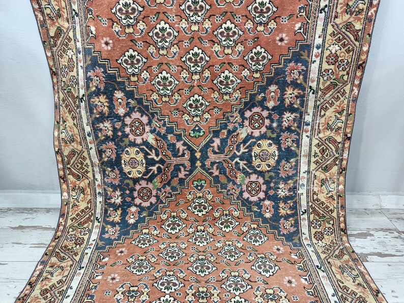 May include: A vintage rug with a traditional Persian design. The rug features a central medallion with intricate floral patterns in shades of red, blue, and cream. The rug has a faded, worn look, adding to its antique charm.
