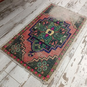 Peut inclure: Un petit tapis rectangulaire avec un motif turc traditionnel. Le tapis est de couleur rose, verte et bleue avec des motifs floraux complexes. Le tapis est effiloch&eacute; sur les bords, ce qui lui donne un aspect vintage.