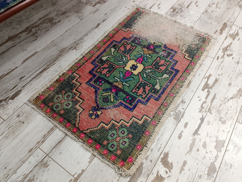 Peut inclure: Un petit tapis rectangulaire avec un motif turc traditionnel. Le tapis est de couleur rose, verte et bleue avec des motifs floraux complexes. Le tapis est effiloch&eacute; sur les bords, ce qui lui donne un aspect vintage.