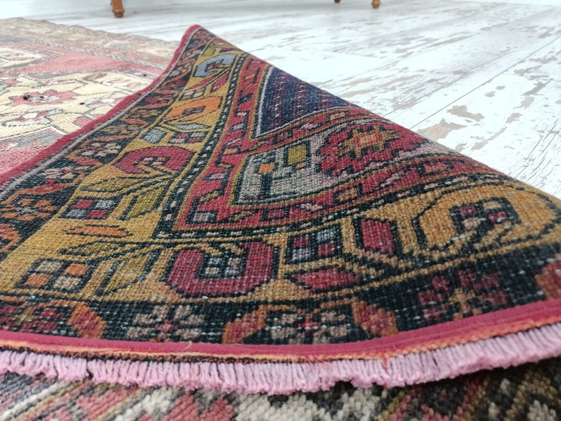May include: A close-up of a colorful, hand-woven rug with intricate patterns in shades of red, yellow, blue, and black. The rug has a pink fringe border.