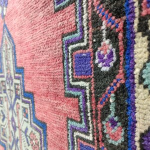 May include: Close-up of a pink, blue, and white patterned rug with a geometric design. The rug has a fringe border.