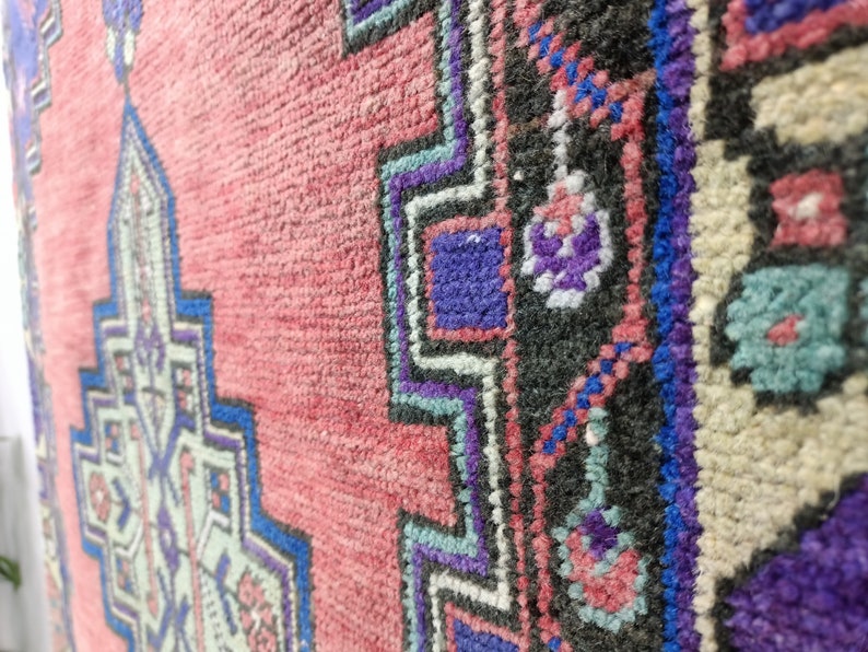 May include: Close-up of a pink, blue, and white patterned rug with a geometric design. The rug has a fringe border.