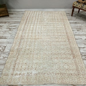 Puede incluir: Una alfombra vintage de color crema con un delicado patr&oacute;n floral de color marr&oacute;n claro. La alfombra tiene un borde con un patr&oacute;n repetitivo.
