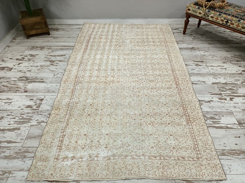 Puede incluir: Una alfombra vintage de color crema con un delicado patr&oacute;n floral de color marr&oacute;n claro. La alfombra tiene un borde con un patr&oacute;n repetitivo.