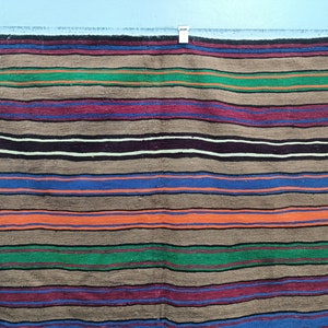 May include: A striped woven throw blanket with brown, blue, green, red, and orange stripes. The blanket is hanging on a wall.