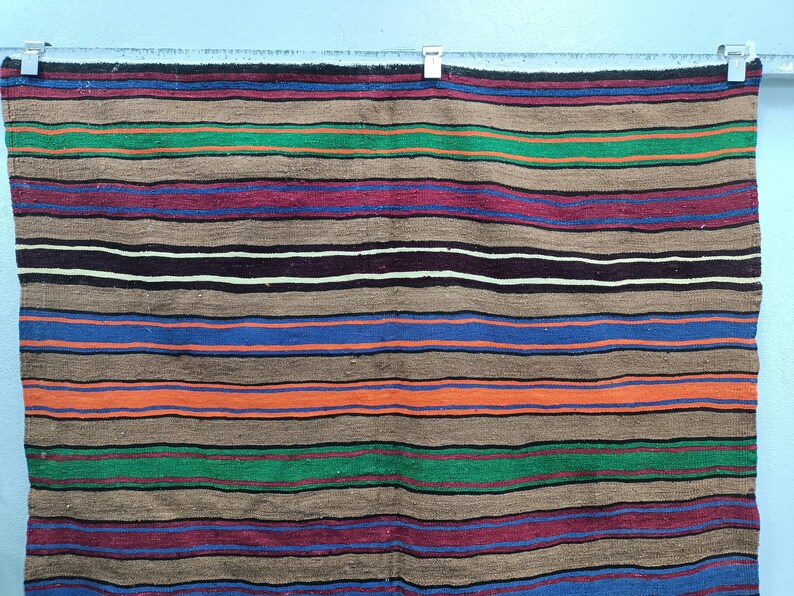 May include: A striped woven throw blanket with brown, blue, green, red, and orange stripes. The blanket is hanging on a wall.
