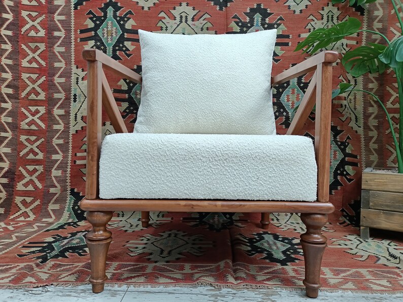 May include: A white armchair with a white fluffy cushion, wooden arms, and turned wooden legs. The chair is in front of a red, black, and white patterned rug.