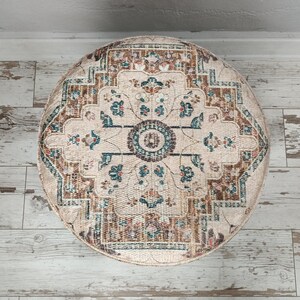May include: A round, cream-coloured rug with a brown, teal and red floral pattern. The rug has a circular design with a central medallion.