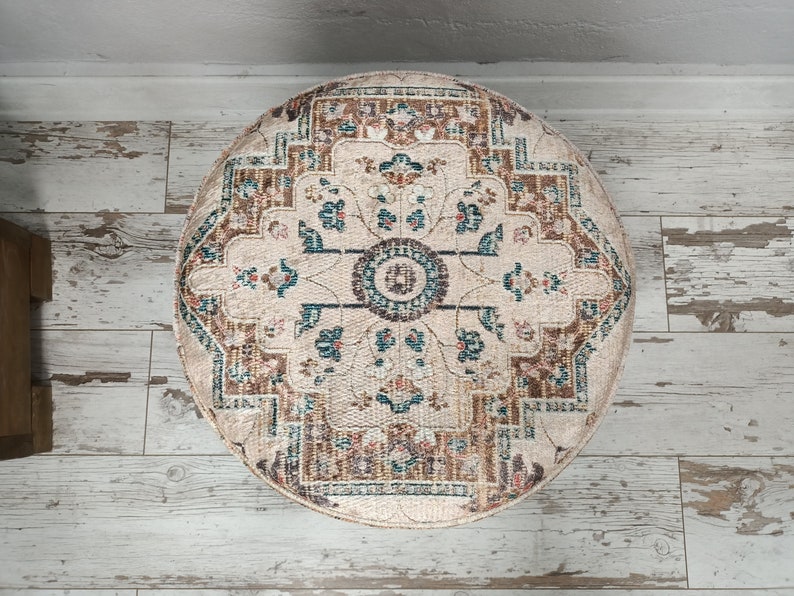 May include: A round, cream-coloured rug with a brown, teal and red floral pattern. The rug has a circular design with a central medallion.